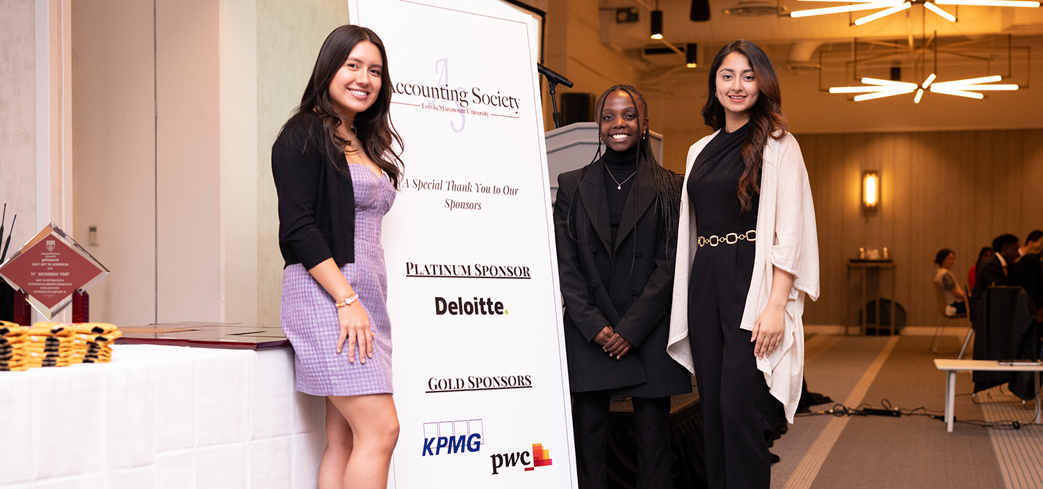 Three students in professional dress in front of a banner with the LMU Accounting Society, Deloitte, KPMG and PwC logos.